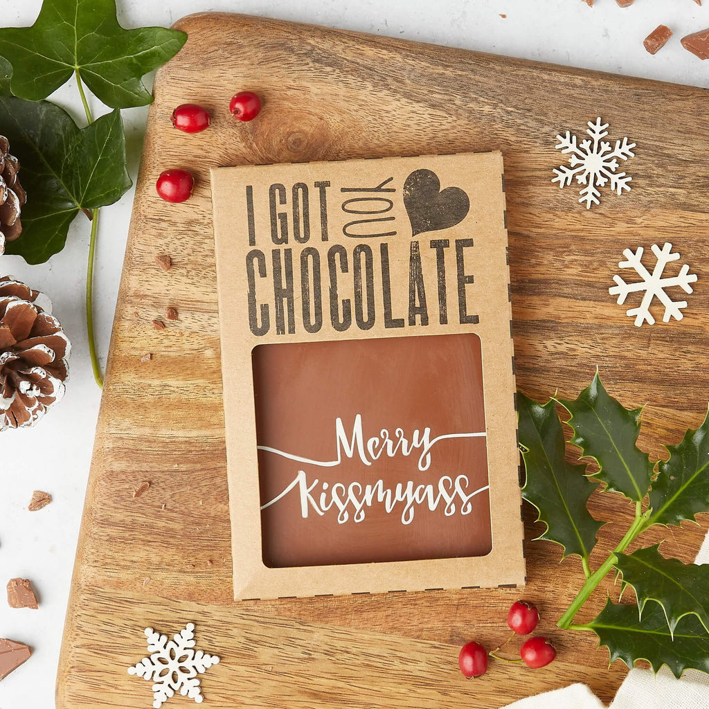 A gift boxed milk chocolate bar that reads “Merry Kissmyass”, amongst festive decor.  Perfect funny stocking fillers for adults who’ve had enough Christmas cheer.