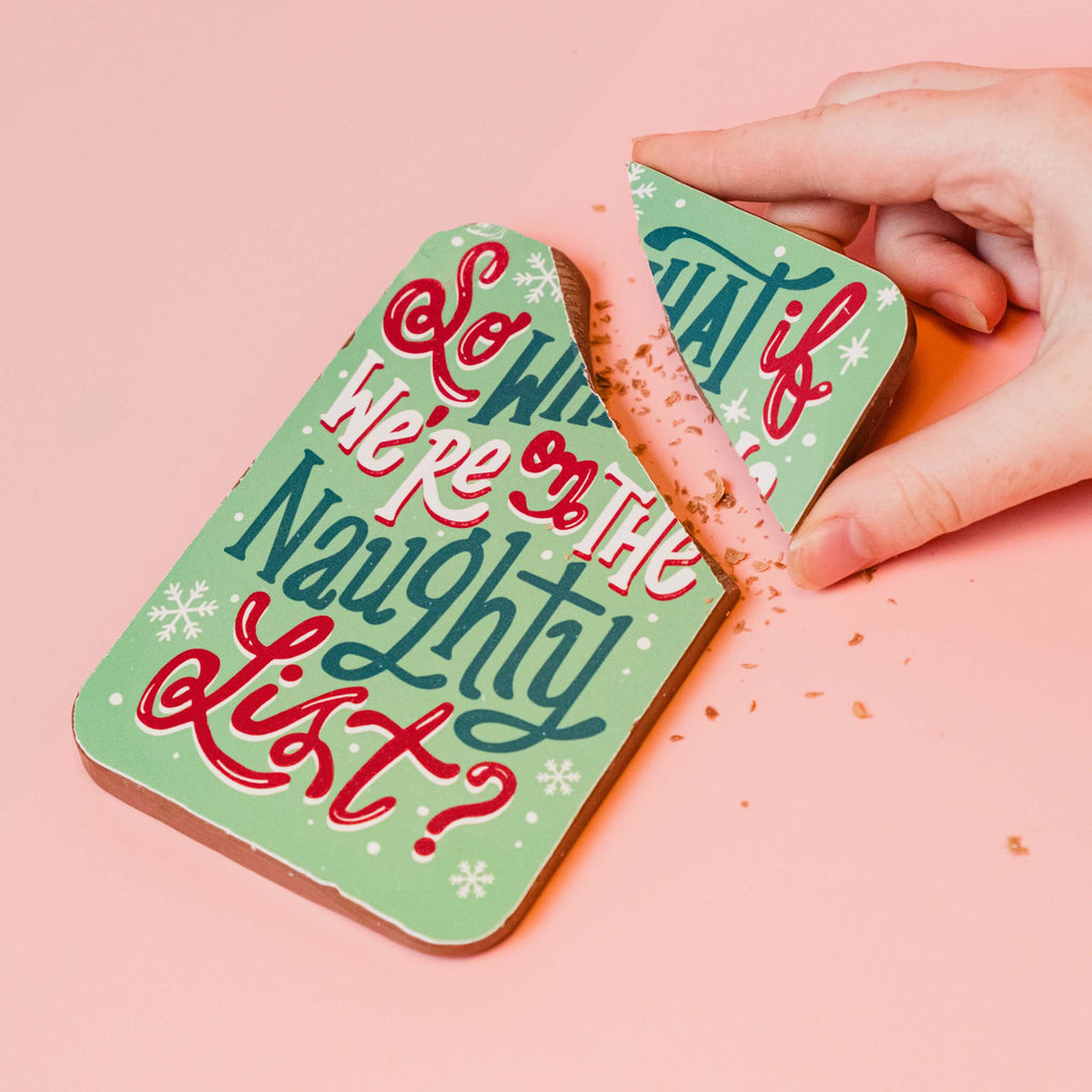 Colourful and festive 'So What if We're on the Naughty List?' milk chocolate bar with a hand breaking the corner off.