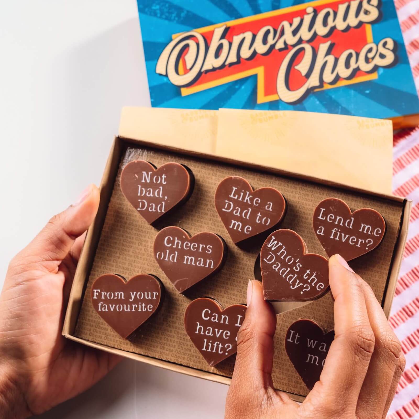 Hands holding a box of Bagstock & Bumble Dad Obnoxious Chocs, packed with chunky Belgian chocolate hearts and sarcastic messages.