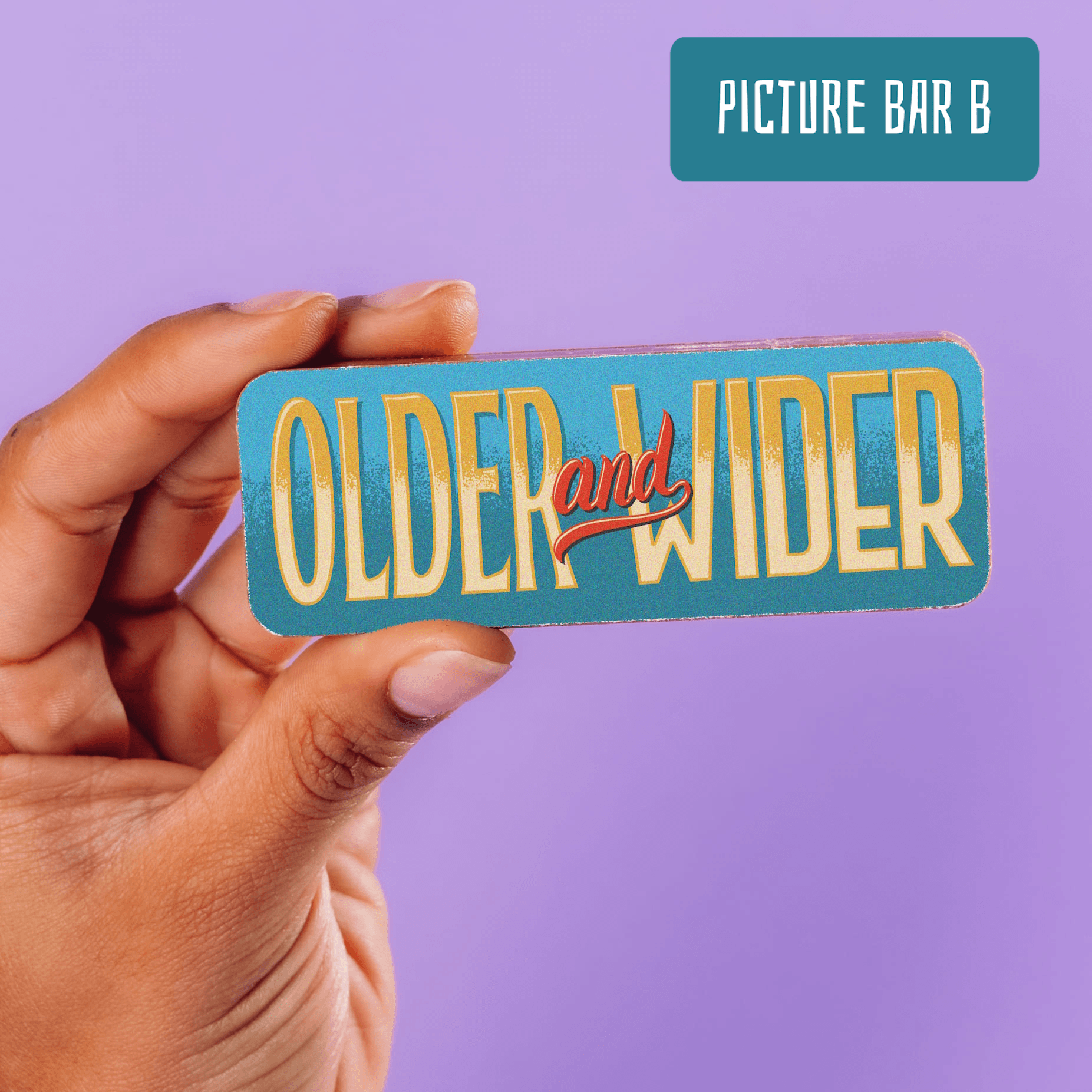 A chocolate bar with a colourful and cheeky 'Older and Wider' slogan being held up.  Part of the Happy Birthday Chocolate Selection Box.