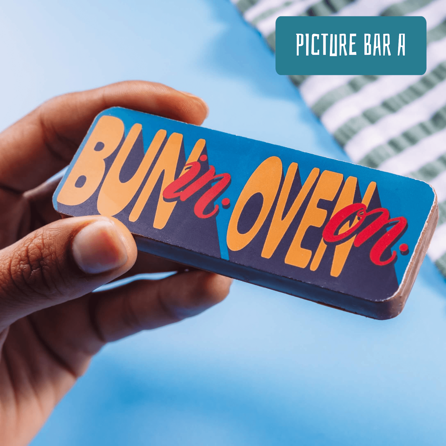 Close-up of a hand holding a chocolate bar that says “Bun in Oven” in bright, playful lettering – one of the best gifts for pregnant women who prefer chocolate over platitudes.