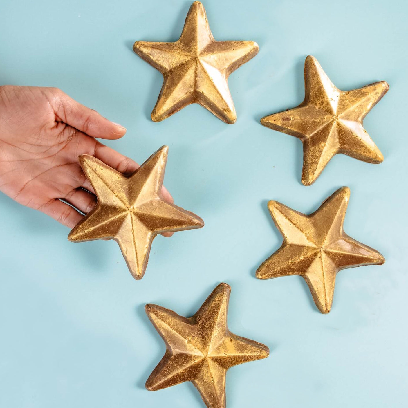 Five gold-dusted chocolate stars arranged on a blue background, with a hand reaching for one – a playful take on chocolate awards for life’s wins.