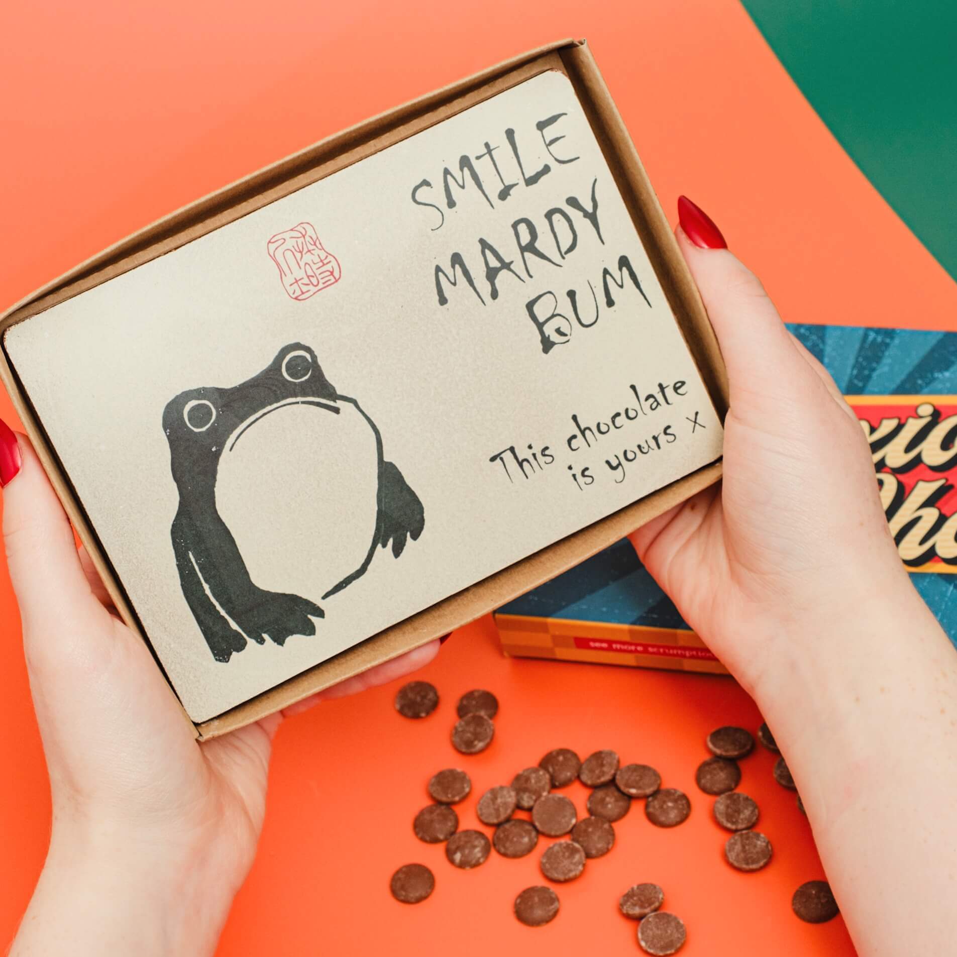 Funny Easter chocolate for adults – a chunky milk chocolate slab with a grumpy cartoon frog and the slogan “Smile Mardy Bum, this chocolate is yours”.