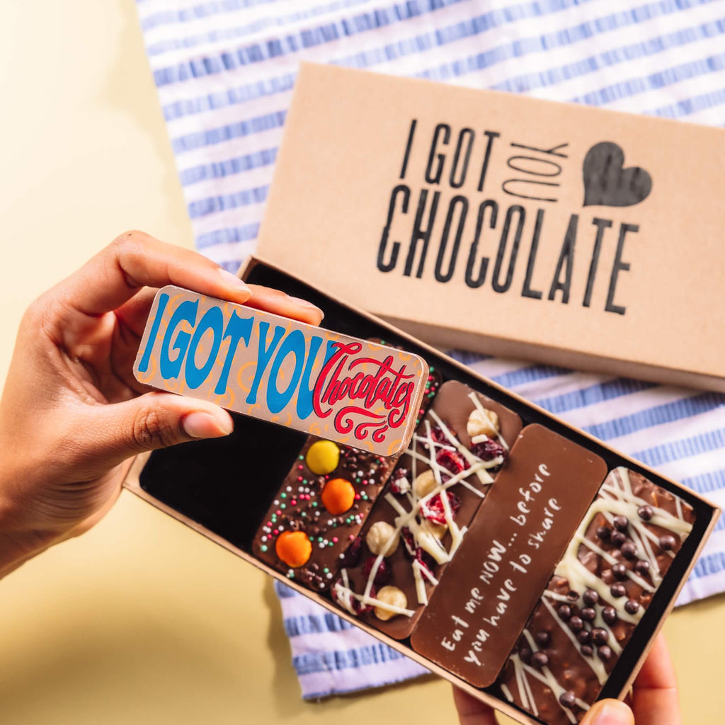 Hand holding up a chocolate bar that says “I Got You Chocolate”, with a gift box of handmade chocolate bars in the background – among the most thoughtful and cheeky I'm sorry gifts