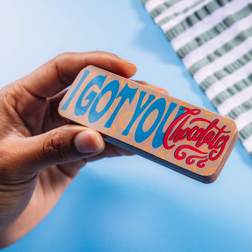 Close-up of a hand holding a chocolate bar that reads “I Got You Chocolate” – a light-hearted choice in gifts to say sorry to a friend.