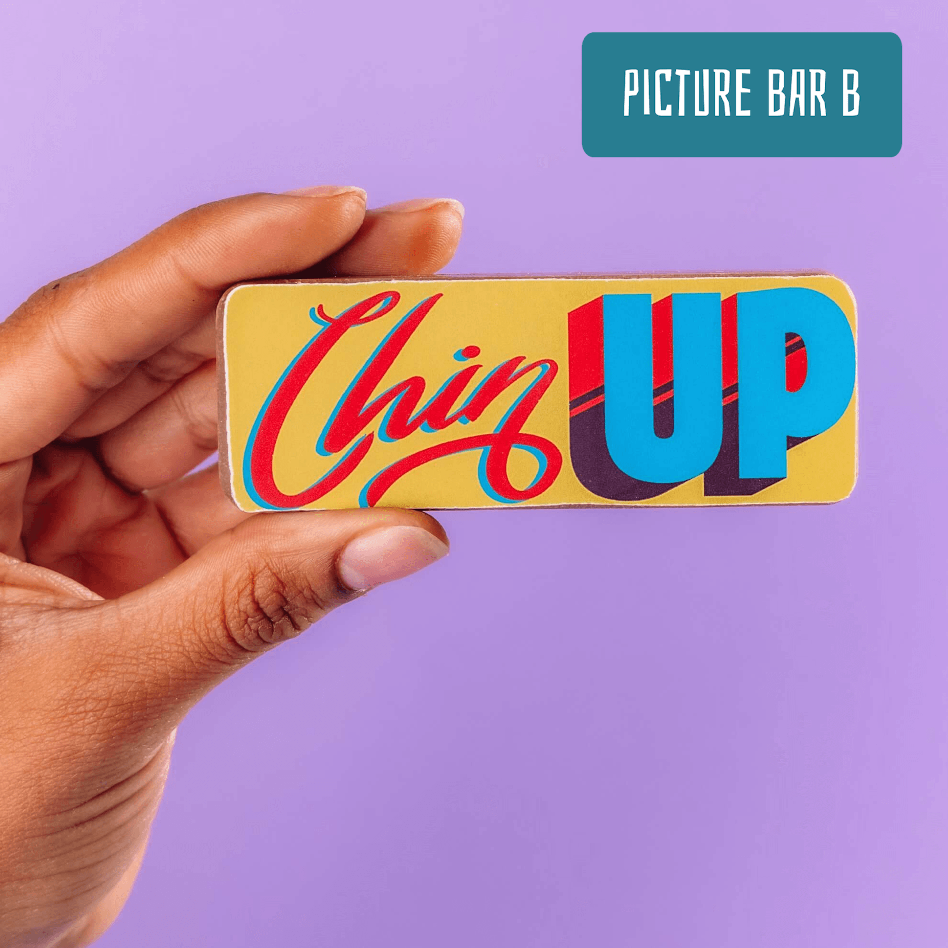 A hand holds a colourfully decorated chocolate bar featuring the words 'Chin UP'.  Part of the chocolate selection apology box.