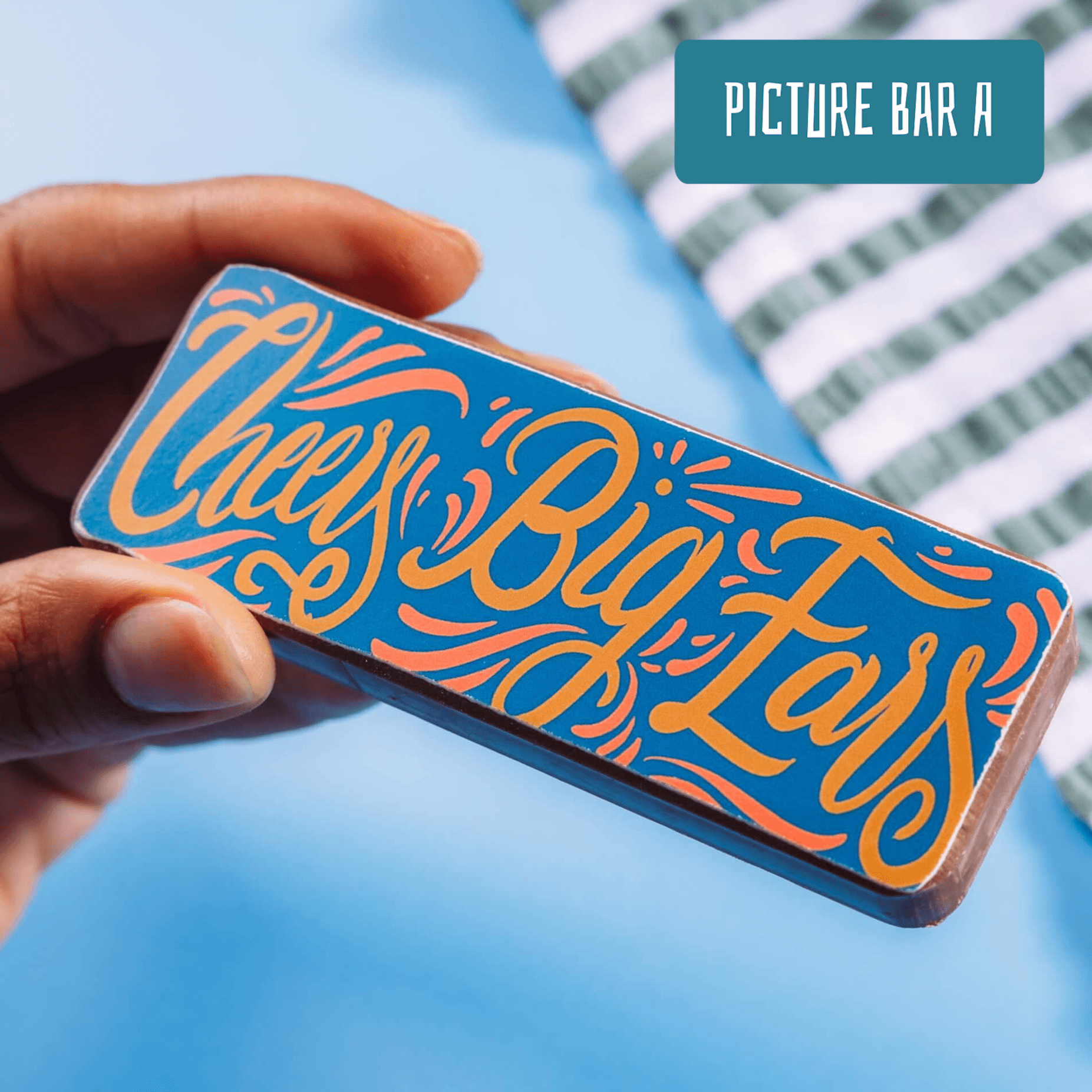 Close-up of a hand holding a bold chocolate bar that reads “Cheers Big Ears” – a playful and edible option among gifts to say thank you for helping.