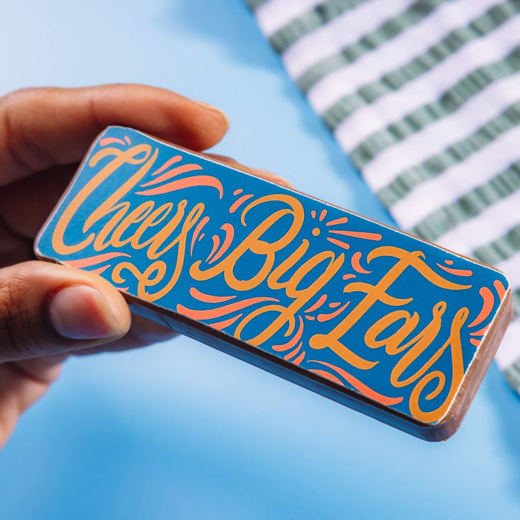 Close-up of a hand holding a bold chocolate bar that reads “Cheers Big Ears” – a playful and edible option among gifts to say thank you for helping.