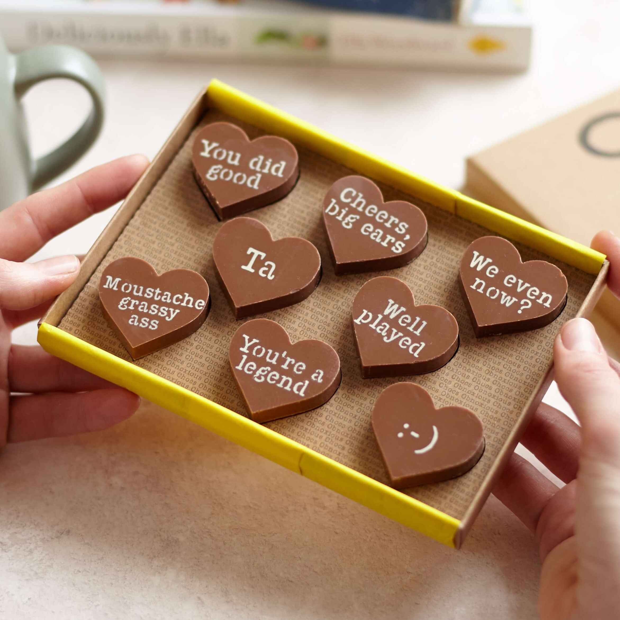 Funny thank you chocolates – A box of Obnoxious Chocs being held up, featuring cheeky messages on chunky Belgian milk chocolate hearts—perfect for a not-so-soppy thank you.