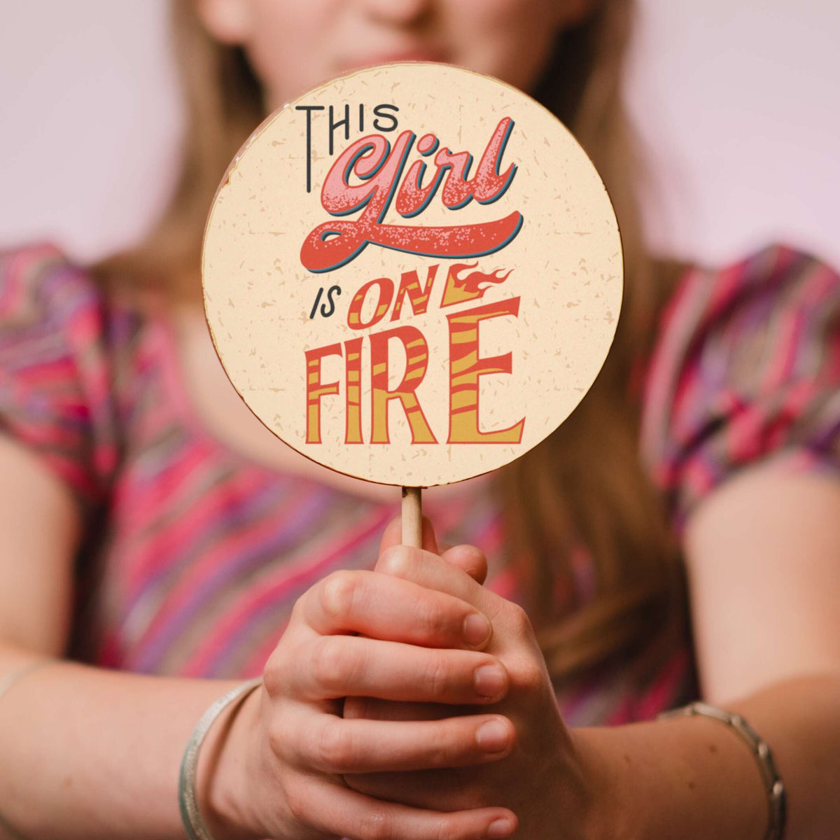A shot of a large, handmade chocolate lolly being held out to the camera – you can see the chunky size and colourful decoration that includes a ‘this girl is on fire’ slogan
