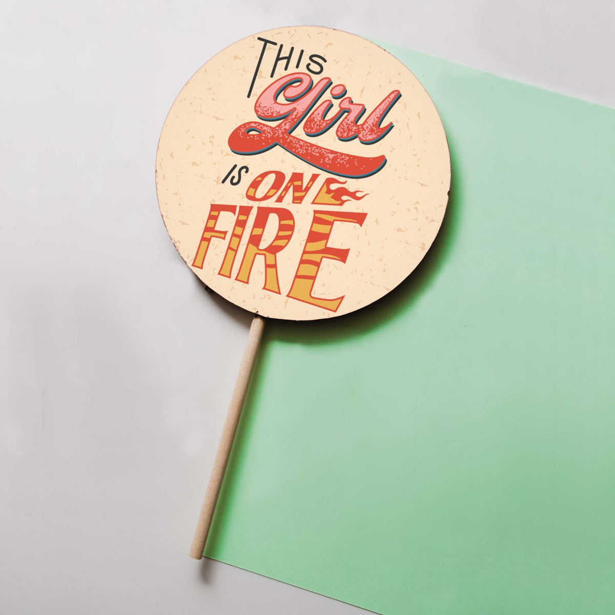 A full view of our giant ‘This girl is on fire’ lolly on it’s wooden stick against a pastel coloured background… a unique and delicious gift for her