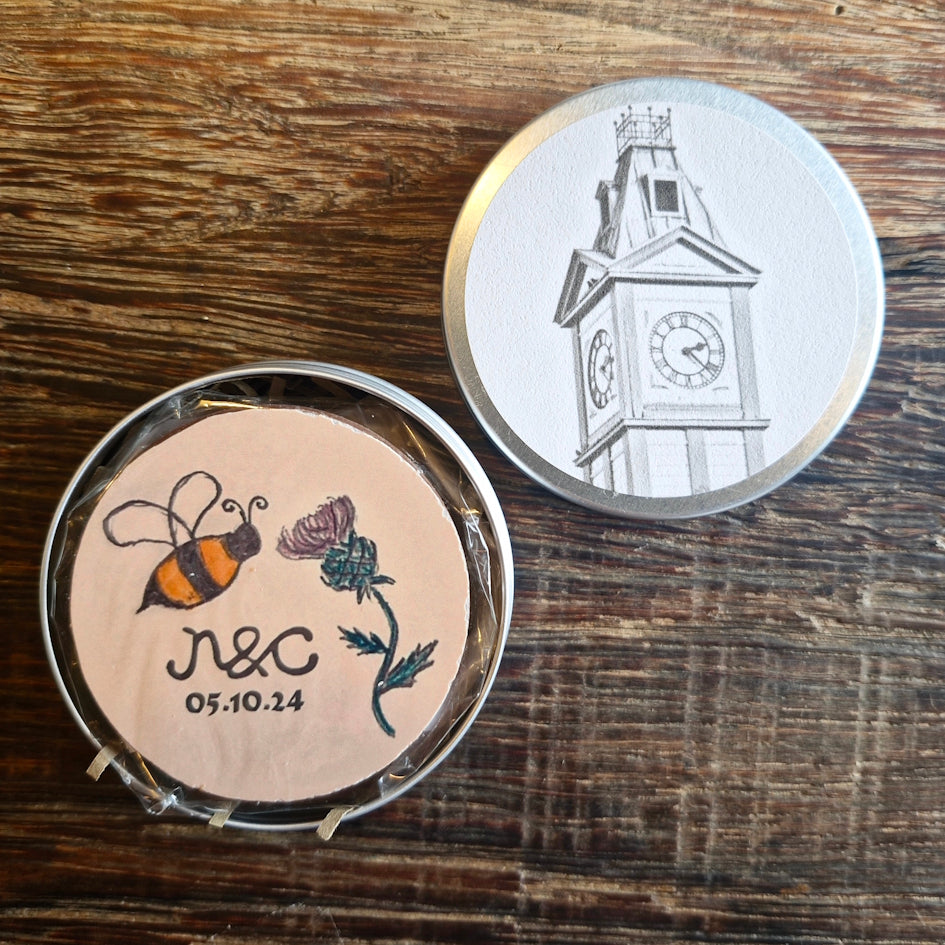 Bespoke wedding chocolate with a a bee and thistle design in a tin with a clock tower illustration.