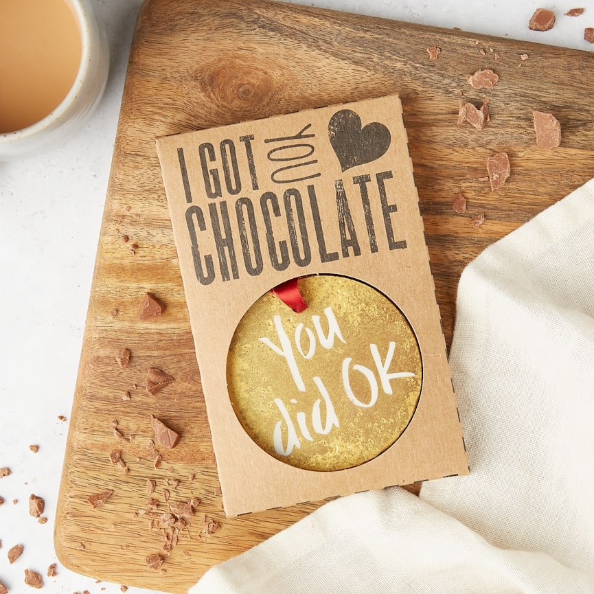 The "You did OK" chocolate medal in its eco-friendly 'I Got You Chocolate' packaging on a wooden board – ideal for insulting gifts to give someone (with love, obviously).