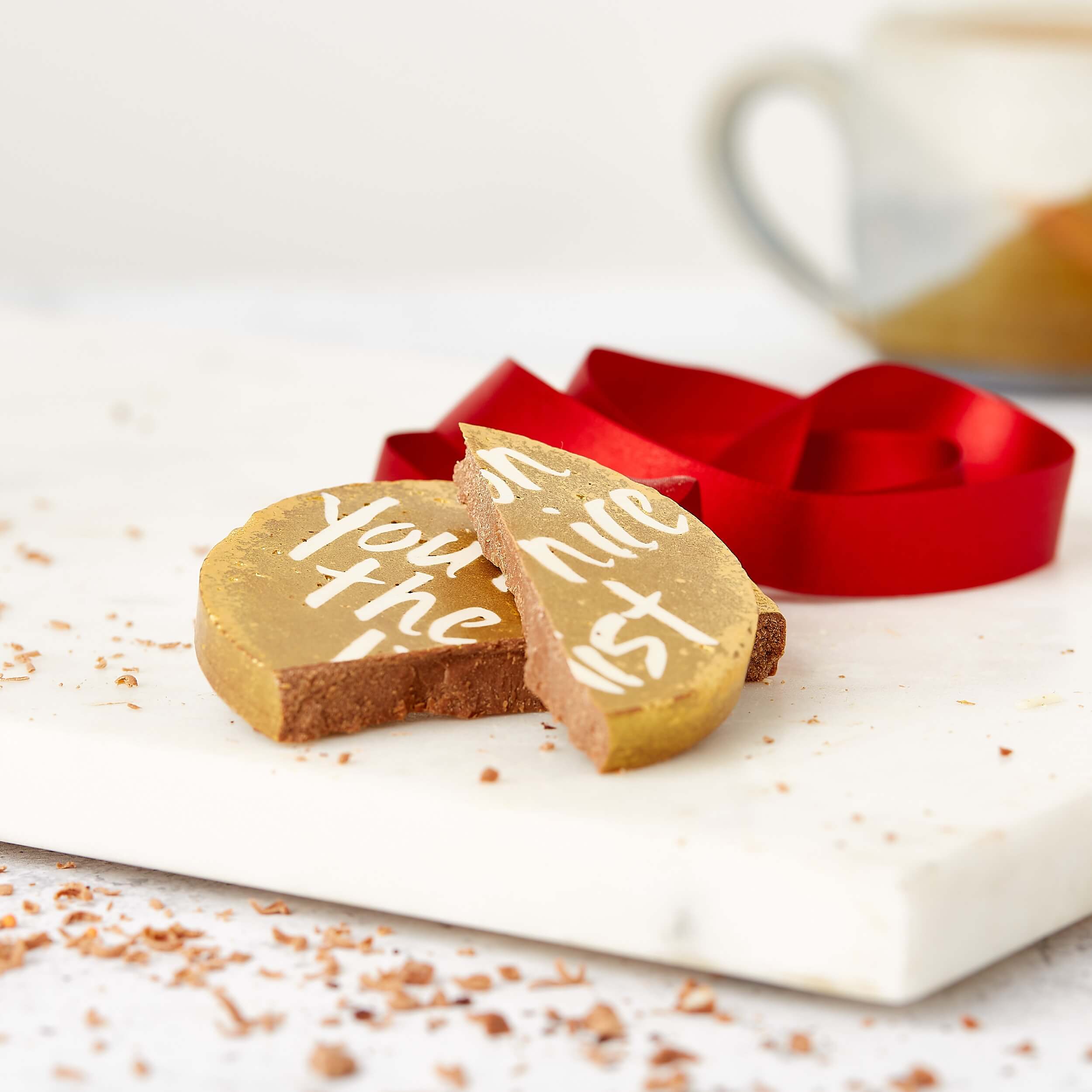 A broken milk chocolate disc reading “You’re on the nice list”, surrounded by shavings and a festive red ribbon – the perfect nice list gift for behaving all year.