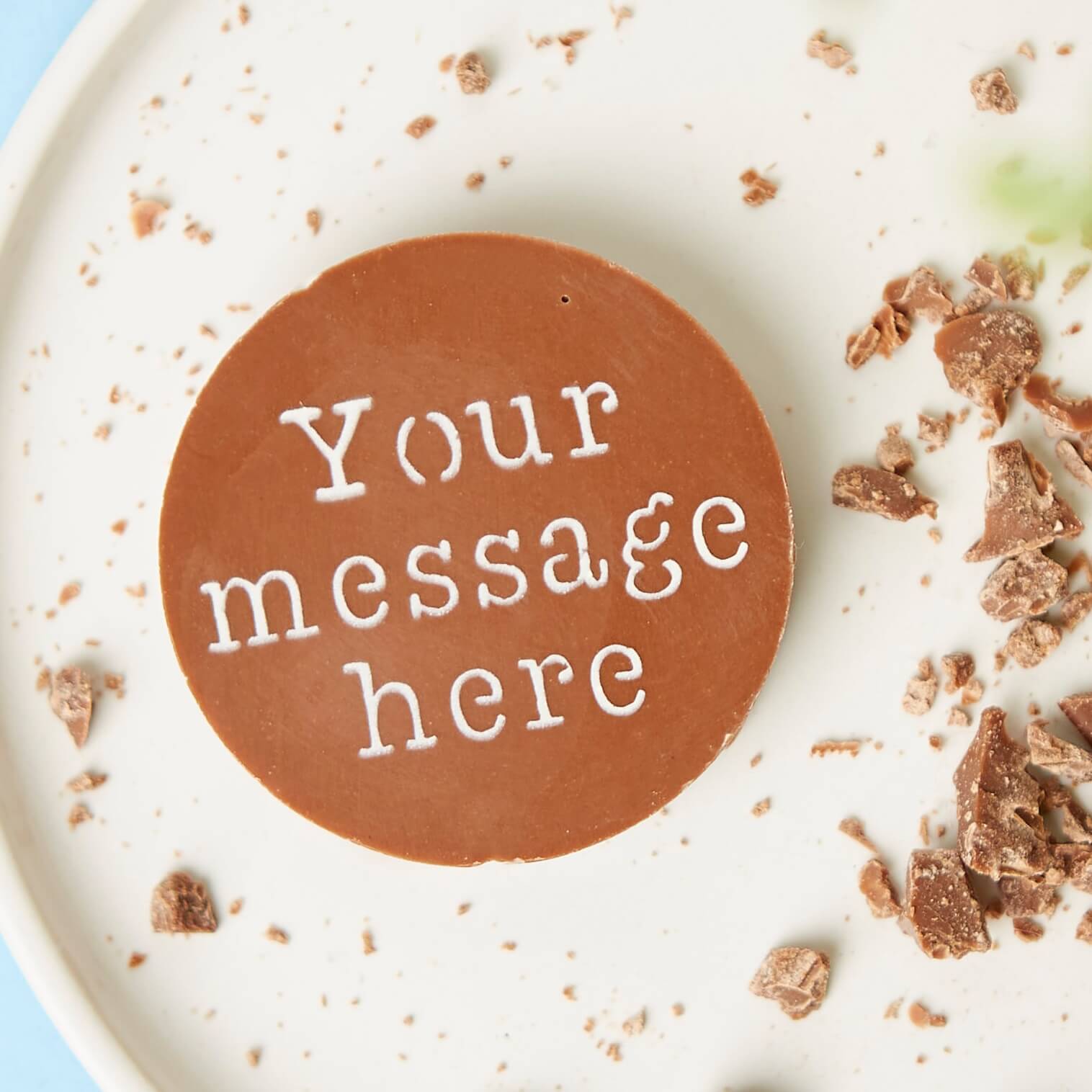 Round chocolate  with 'Your message here' text on a white plate with crumbled chocolate in the background