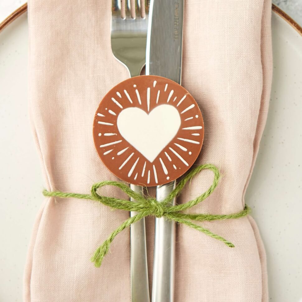 Circular chocolate decorated with a heart starburst design pictured on a place setting.