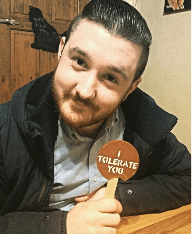 Man holding a chocolate lolly saying 'I Tolerate You' in a casual setting
