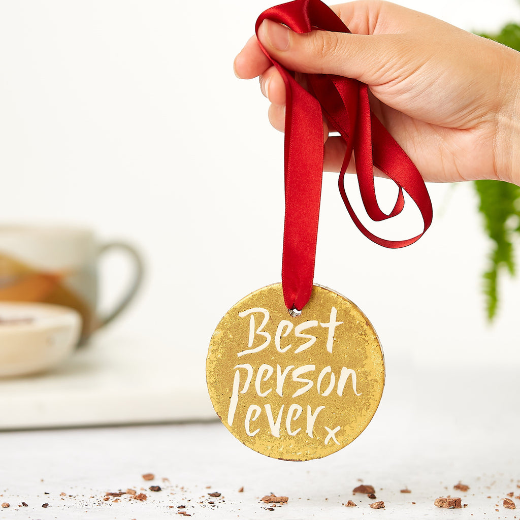 A hand holding a chocolate gold medal hanging from a red ribbon.  The medal is decorated with a 'Best person ever' message