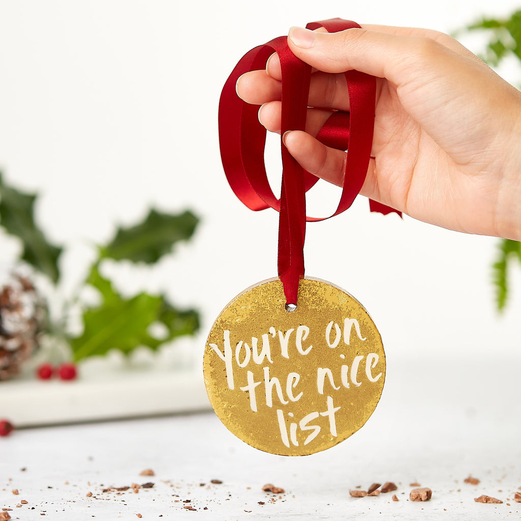 Shimmery gold chocolate stocking filler, hanging from a red ribbon and decorated with a 'You're on the nice list' message