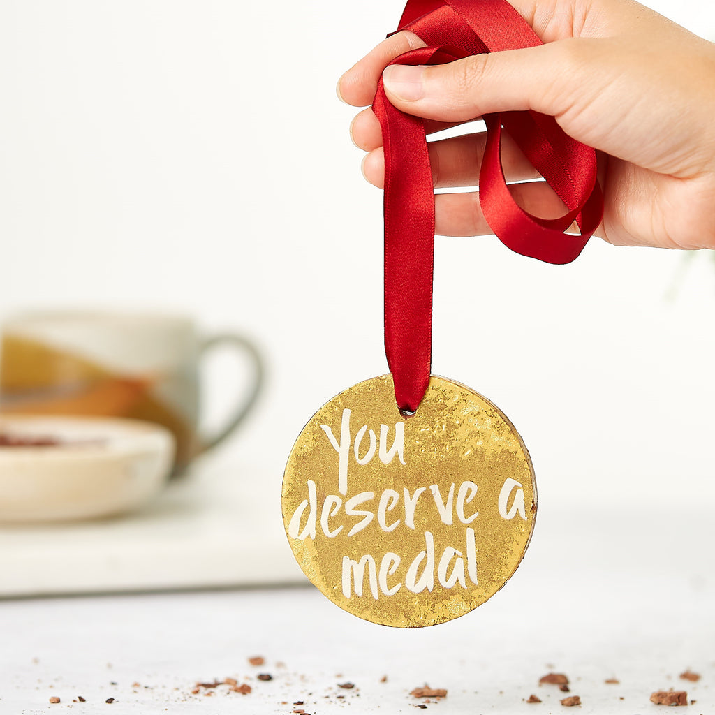 Shimmery gold 'You deserve a medal' chocolate medal being held up by it's red ribbon