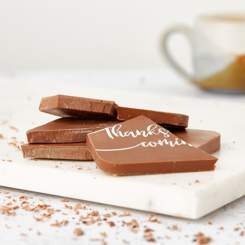 Broken chunks of Belgian chocolate bar decorated with a coloured cocoa butter message that says 'Thanks for coming'